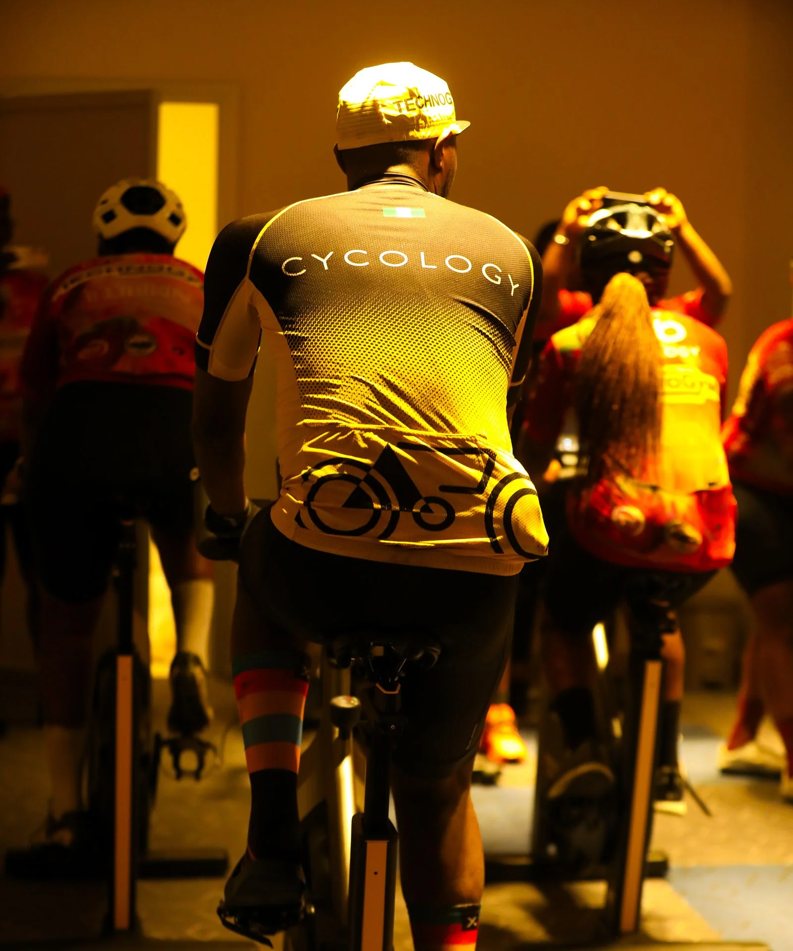 Riders on indoor bikes in a warmly lit cycling studio